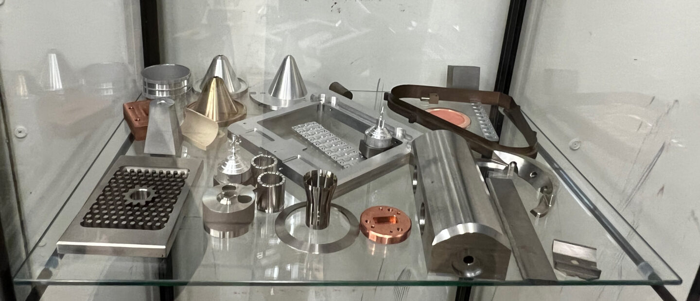 Collection of precision-machined metal components displayed on a glass shelf