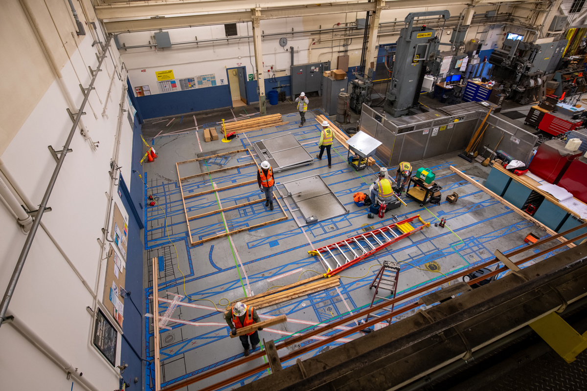 Aerial perspective of workers preparing installation site for new CNC machine on a shop floor with blue layout markings