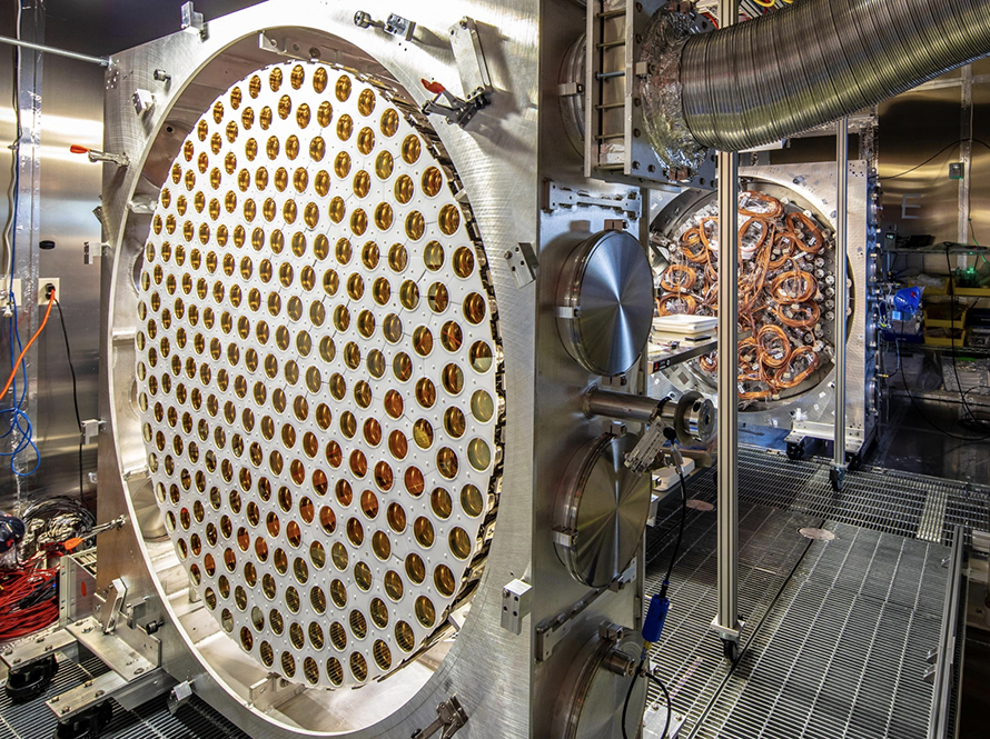 Large circular detector panel with hundreds of gold-colored sensor ports in an equipment room.