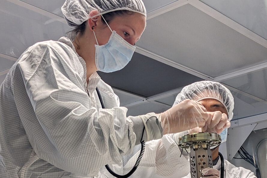 Two researchers in PPE installing the central bearing assembly for the rotating carousel mechanism