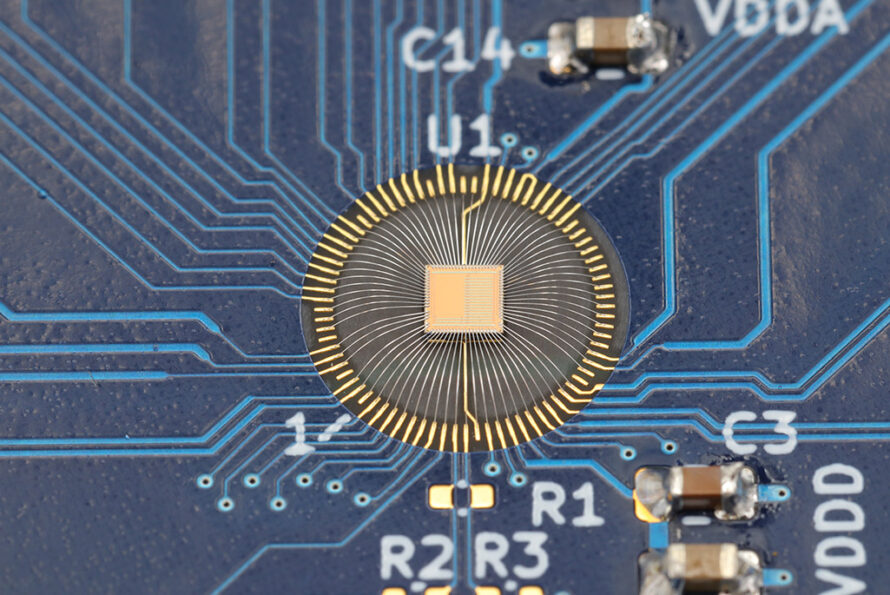 Close-up of chip with radial gold bond wires connecting to blue circuit board