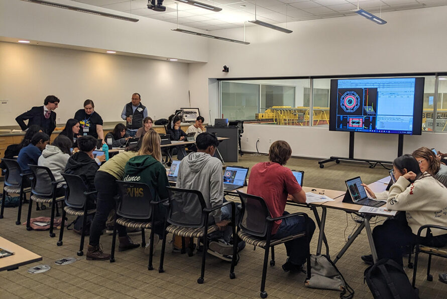 Students working on their laptops in a classroom while Lab volunteers provide assistance