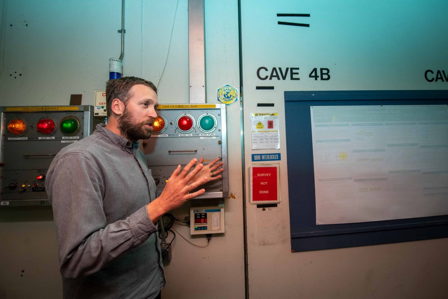 A scientific engineering associate stands in front of an equipment panel with lights and talks to high school students