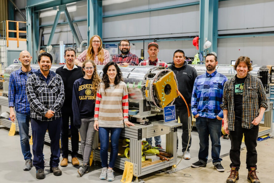 A group of researchers and engineers pose around a magnet