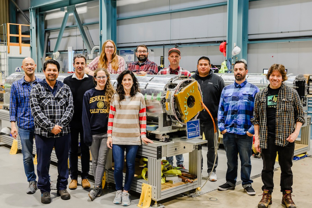 A group of researchers and engineers pose around a magnet