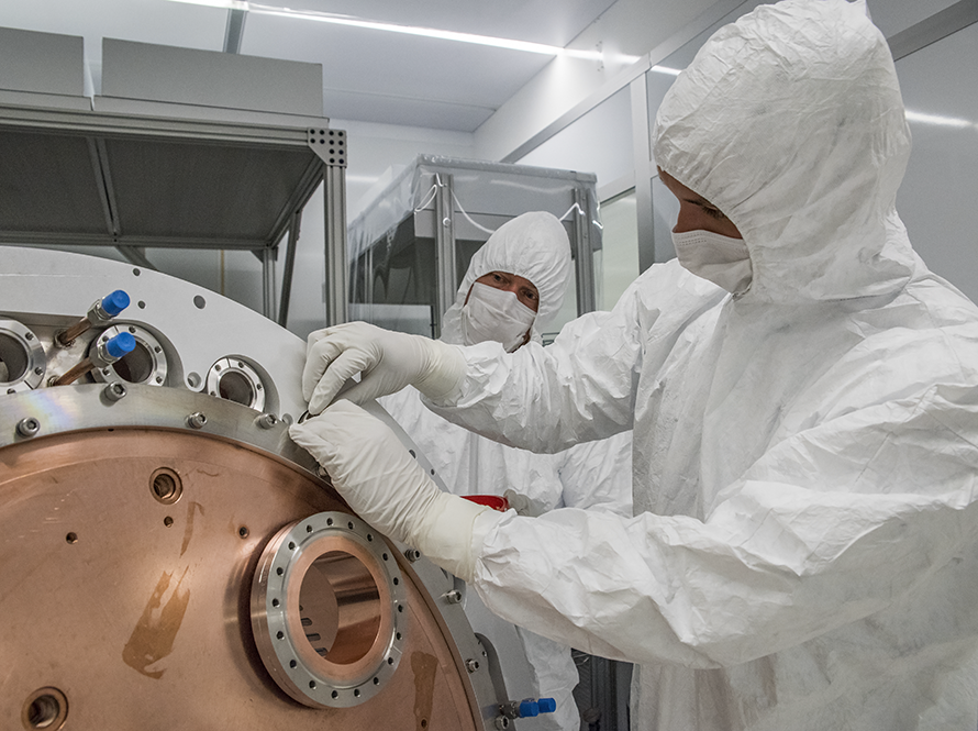 Cleanroom scene showing two workers in protective suits and face coverings working on equipment