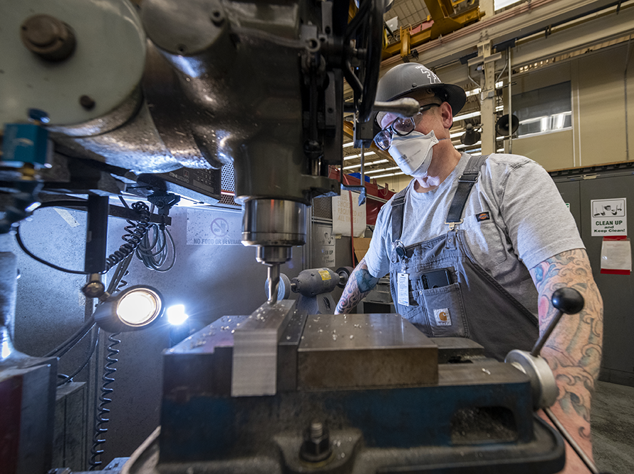 Engineer working in the metal shop with large drill with light behind.