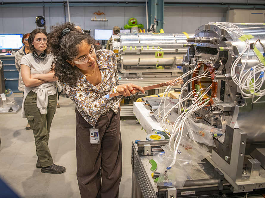An engineering associate showing students how superconducting magnets are built.