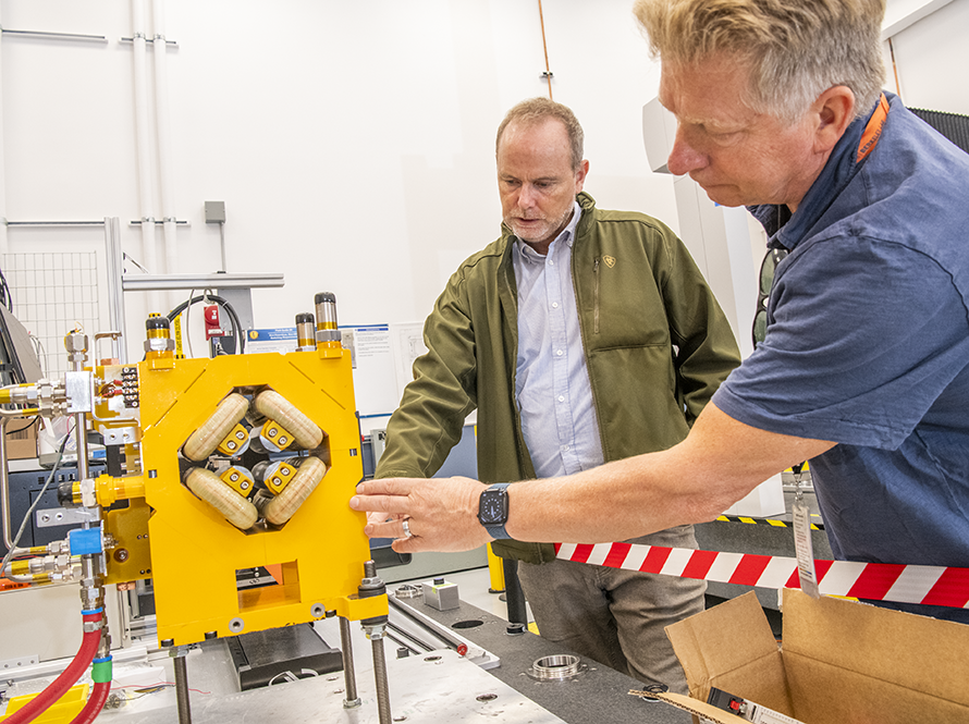 Two engineers examining yellow laboratory testing equipment for ALS-U.