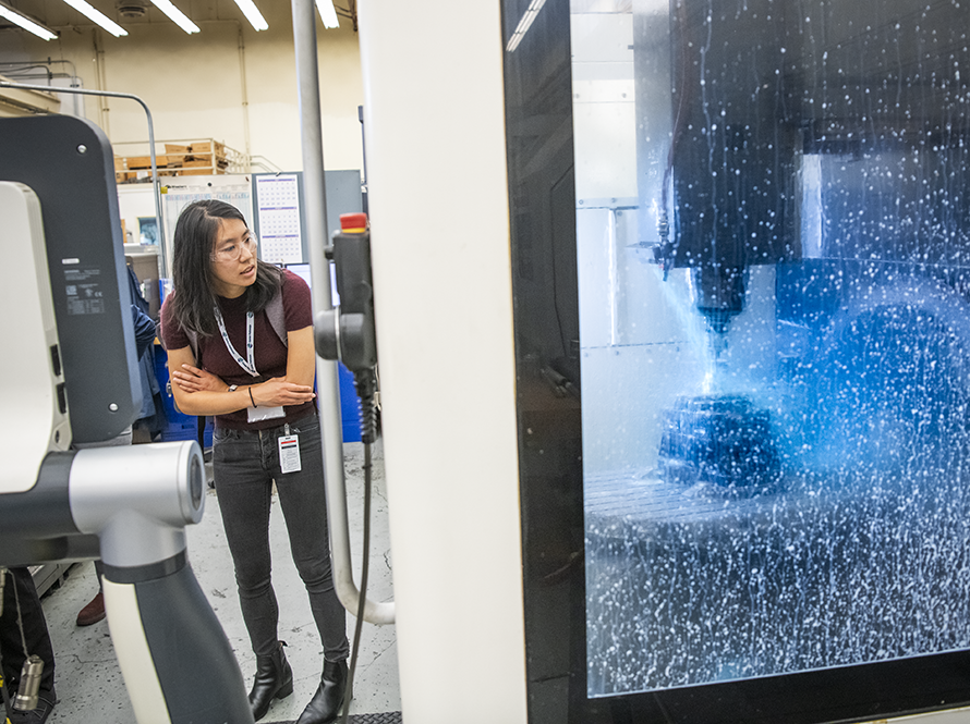 An engineer observes machining operation through protective glass enclosure.