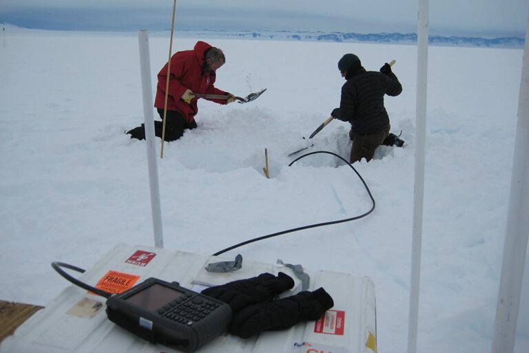 Two researchers digging antenna holes at their camp on the Ross Ice Shelf.