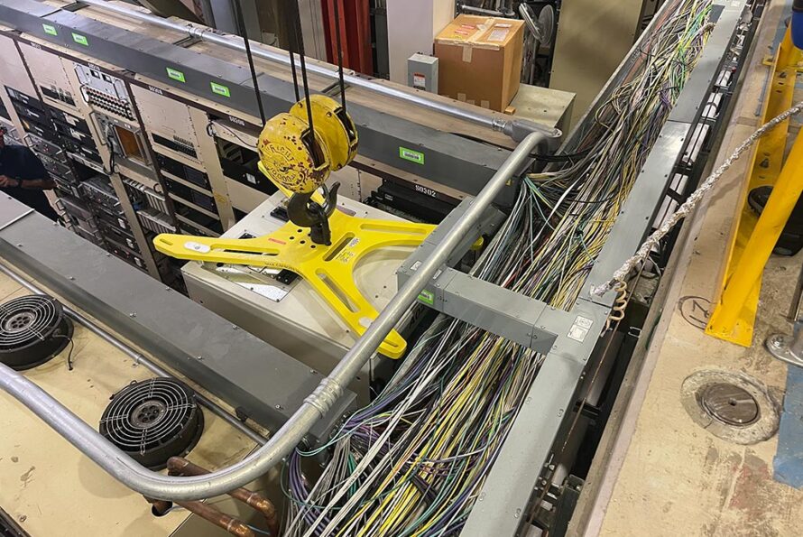 Close-up view of yellow X-shaped lifting fixture attached to top of equipment rack during crane operation in ALS