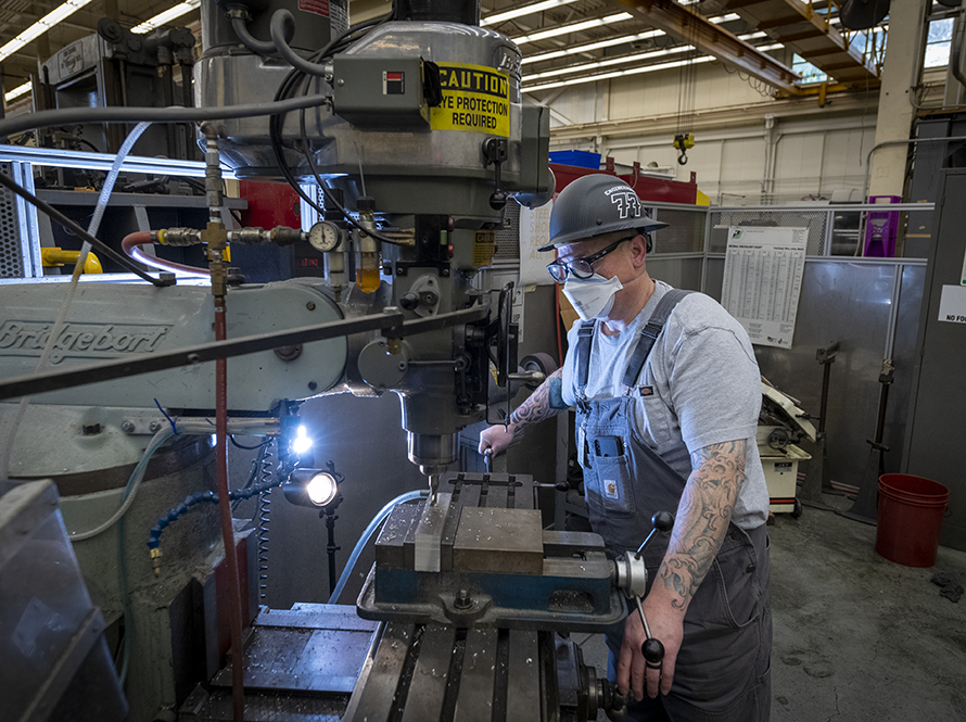 Machinist in PPE working on component fabrication in the workshop.