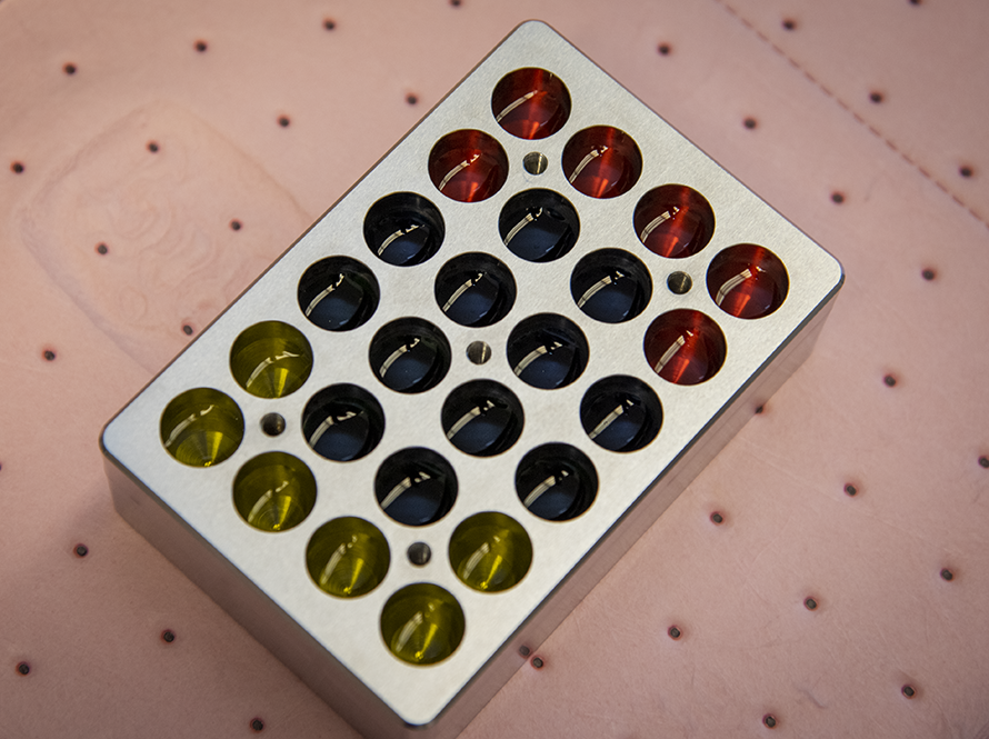 Metal sample holder with cylindrical wells holding color-tinted components.