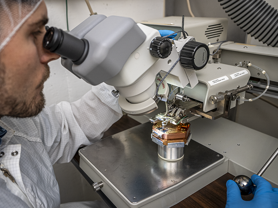 An engineer looking at circuit components under a microscope.
