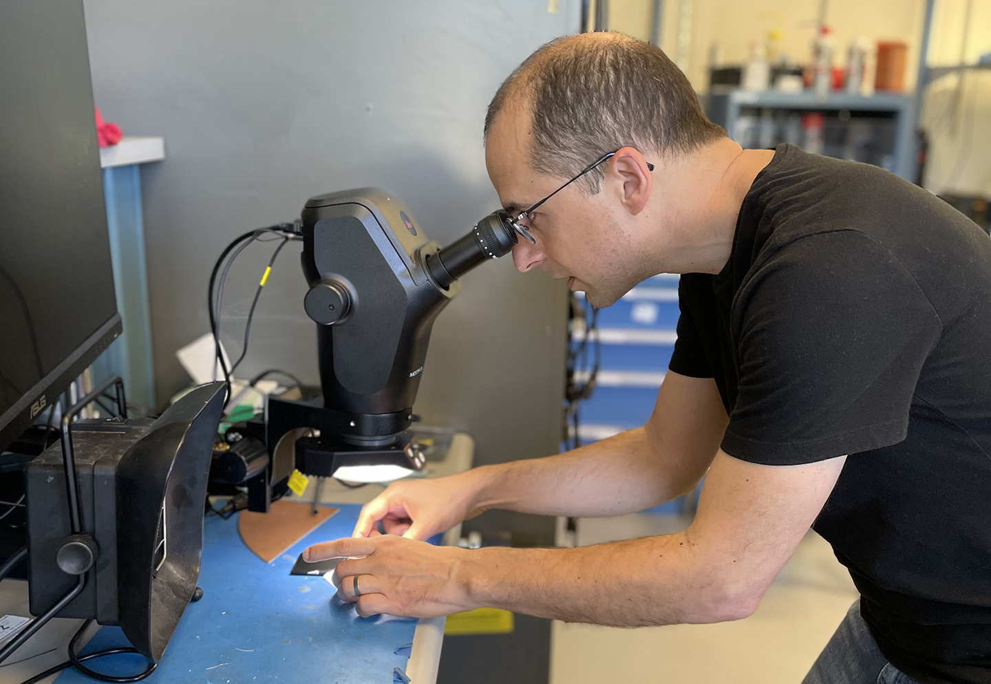 A man peers into a microscope while examining microchips.