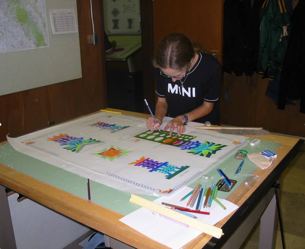 Jennifer Doyle leaning over a table, using drafting tools to work on a technical drawing.