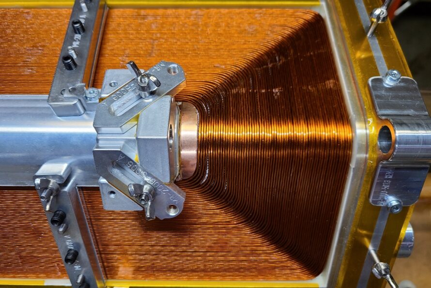 A completed closed-loop coil showing a continuous strand of Nb-Ti superconducting wire wound around a hexagonal mandrel.