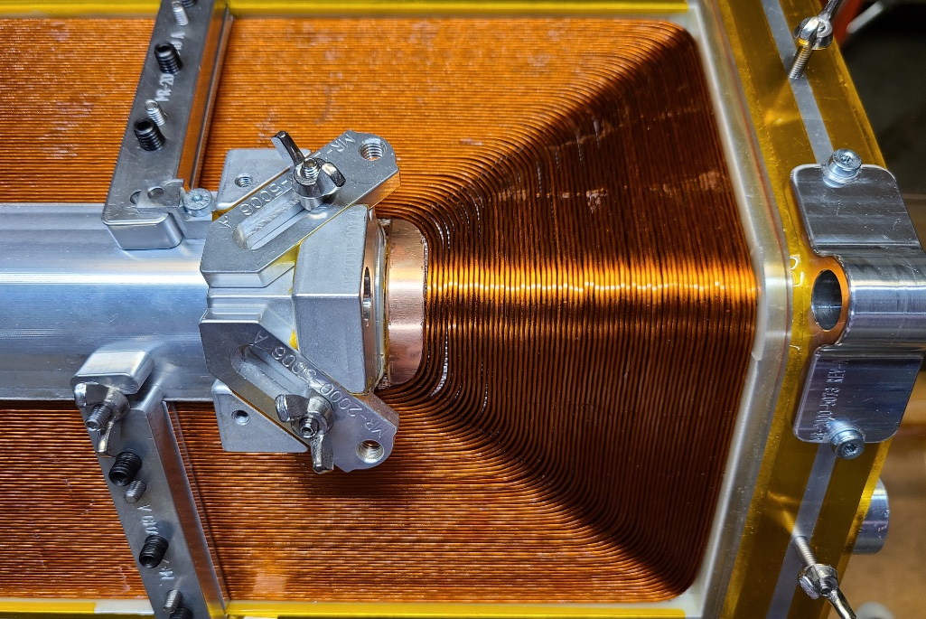 A completed closed-loop coil showing a continuous strand of Nb-Ti superconducting wire wound around a hexagonal mandrel.