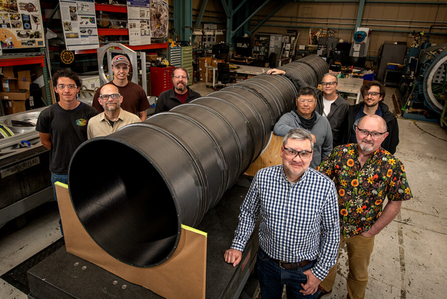 The ATLAS Pixel Support Tube builders and fabricators, photographed next to the Pixel Support Tube, in the Engineering Division's Mechanical Fabrication Shops (April 2026).