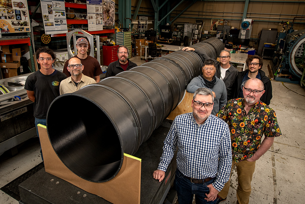 The ATLAS Pixel Support Tube builders and fabricators, photographed next to the Pixel Support Tube, in the Engineering Division's Mechanical Fabrication Shops (April 2026).