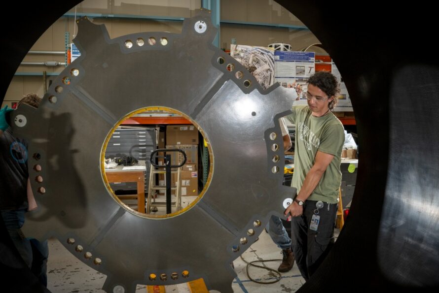 Mechanical Technician Marcos Toledo McGee lifts a component of the ATLAS Detector carbon fiber cylinder into place in the Engineering Division’s shop facility.