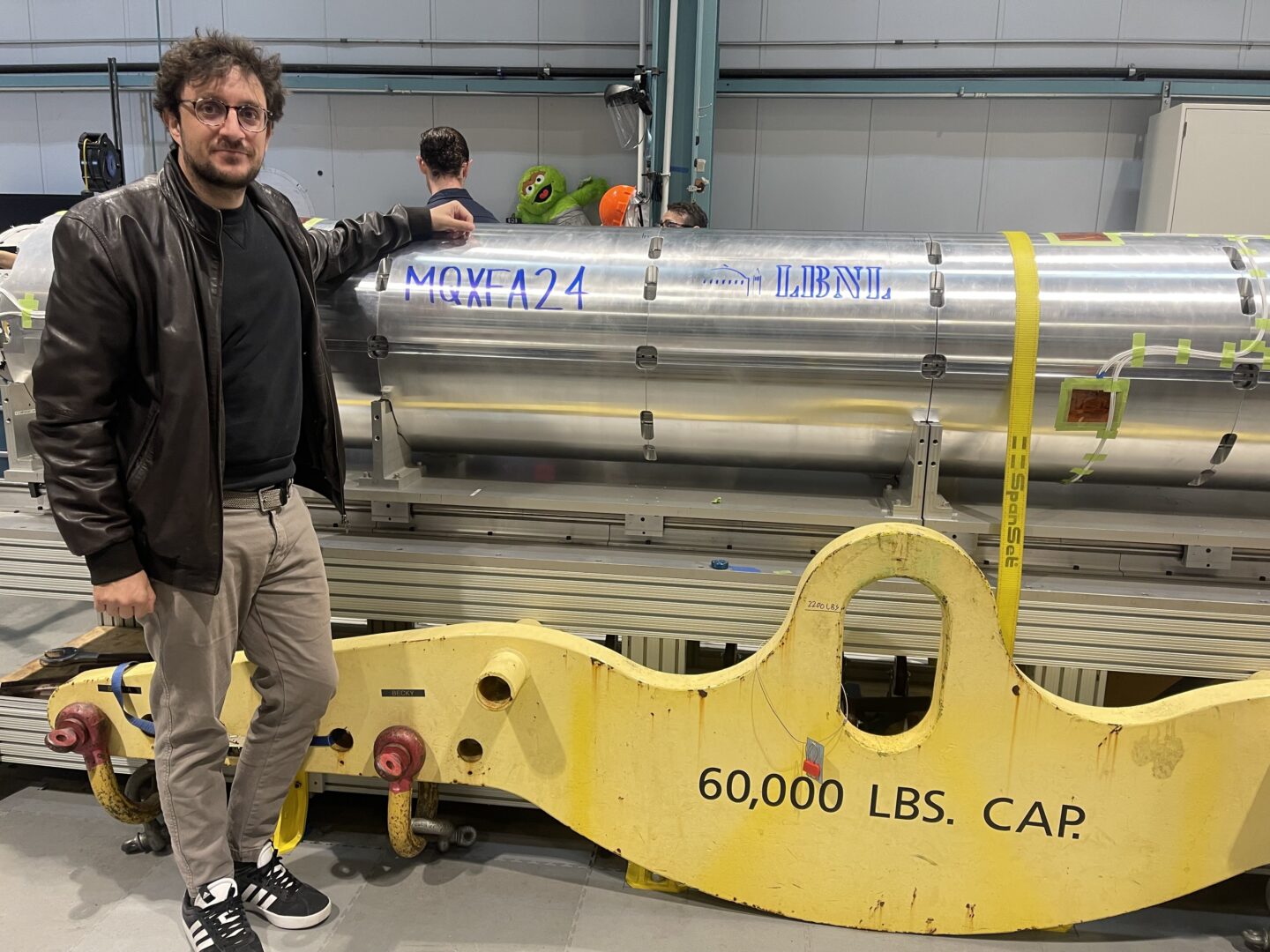 Vallone stands next to a MQXFA magnet at Berkeley Lab. This magnet was assembled by BCMT staff from the Engineering and ATAP Divisions for the High Luminosity Large Hadron Collider (HL-LHC) upgrade at CERN.